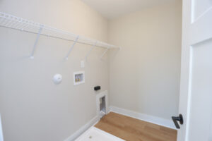 Empty laundry room with wooden floor, wall hooks, and space for washer and dryer in Poplar Villages Lot 1.