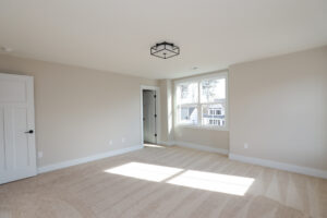 Empty room in Poplar Village with beige carpet, large window, white walls, and a modern ceiling light fixture.