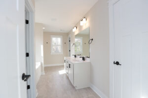 Bright bathroom in Lot 1, Poplar Village, with dual sinks, large mirror, and sunlight streaming through a window near the tub.