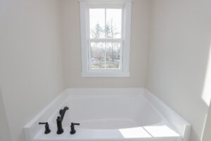 A white bathtub beneath a window with black fixtures offers an outdoor view in Poplar Village, Lot 1.