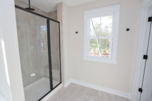 Minimalist bathroom in Poplar Villages Lot 1, featuring a glass shower, tiled floor, and a window with white trim.