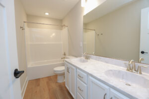 Bright bathroom in Poplar Village with a double sink vanity, large mirror, bathtub, and wood-look flooring.