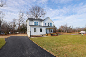 A white two-story house with a black roof on Lot 1 in Poplar Village, surrounded by a grassy lawn and black driveway.