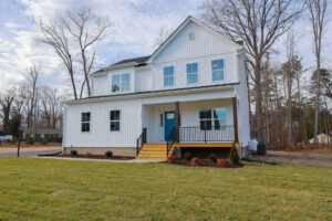 A modern two-story white house with a front porch, nestled in Poplar Villages Lot 1, surrounded by a grassy yard and trees.