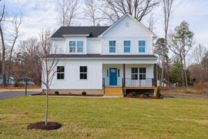 Nestled in Poplar Village, Lot 1 is a two-story white house with a blue door, surrounded by lush grass and trees.