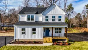 Two-story white house with a blue door on Lot 1, featuring a black roof and wooden porch in Poplar Villages serene setting.