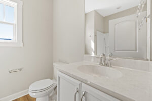 Nestled in Poplar Village, this minimalist bathroom in Lot 1 features a white sink, marble countertop, and toilet. Sunlight streams through a nearby window, enhancing the serene ambiance.