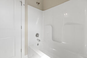 A white bathtub with a built-in wall surround and chrome fixtures graces the bathroom in Lot 1 of Poplar Village, set beside a pristine white door.