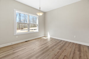 The empty room in Poplar Village features a wooden floor, a large window, and a hanging light fixture. Its light-colored walls add to the serene ambiance of this Lot 1 gem.