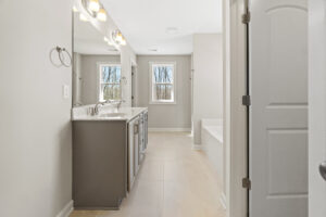 Modern bathroom in Poplar Village's Lot 1, featuring a large mirror, dual sinks, and natural light streaming through two windows. It boasts a neutral color scheme for a serene ambiance.