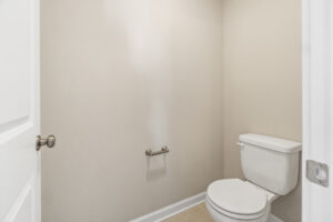 Minimalist bathroom in Poplar Village with an empty toilet paper holder, white toilet, and beige walls.