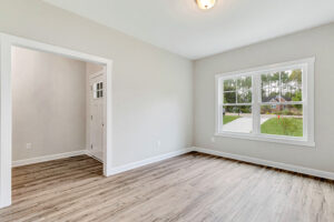 Bright empty room with wood floors, large window, white trim, and view of greenery outside.