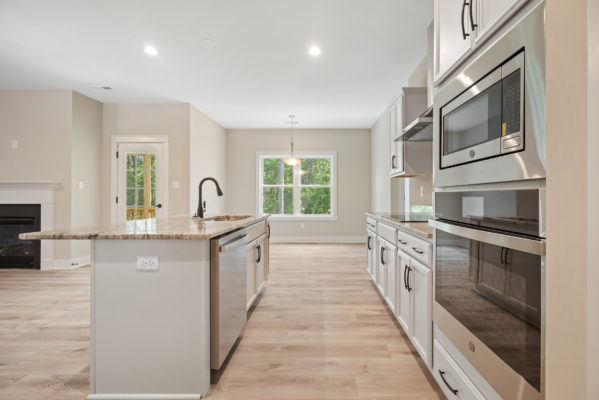 Modern kitchen in new Virginia home with stainless steel appliances, island sink, and views of dining area and outdoor greenery.