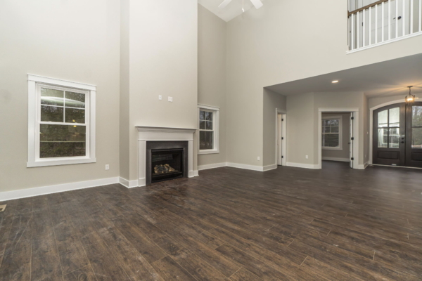 Spacious empty room with hardwood floors, fireplace, and large windows in a high-ceiling new home with balcony views.