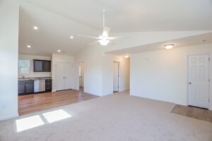 Bright open living area with carpet, ceiling fan, and view of kitchen with wood flooring and cabinets.