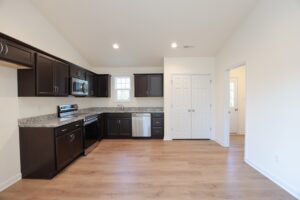 Modern kitchen with dark cabinets, stainless steel appliances, wood floor, and white walls.