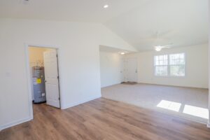 Bright living room with ceiling fan, carpet, large window, and adjacent room with a water heater visible.