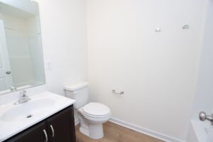 A clean, white bathroom with a sink, toilet, and light wood floor.