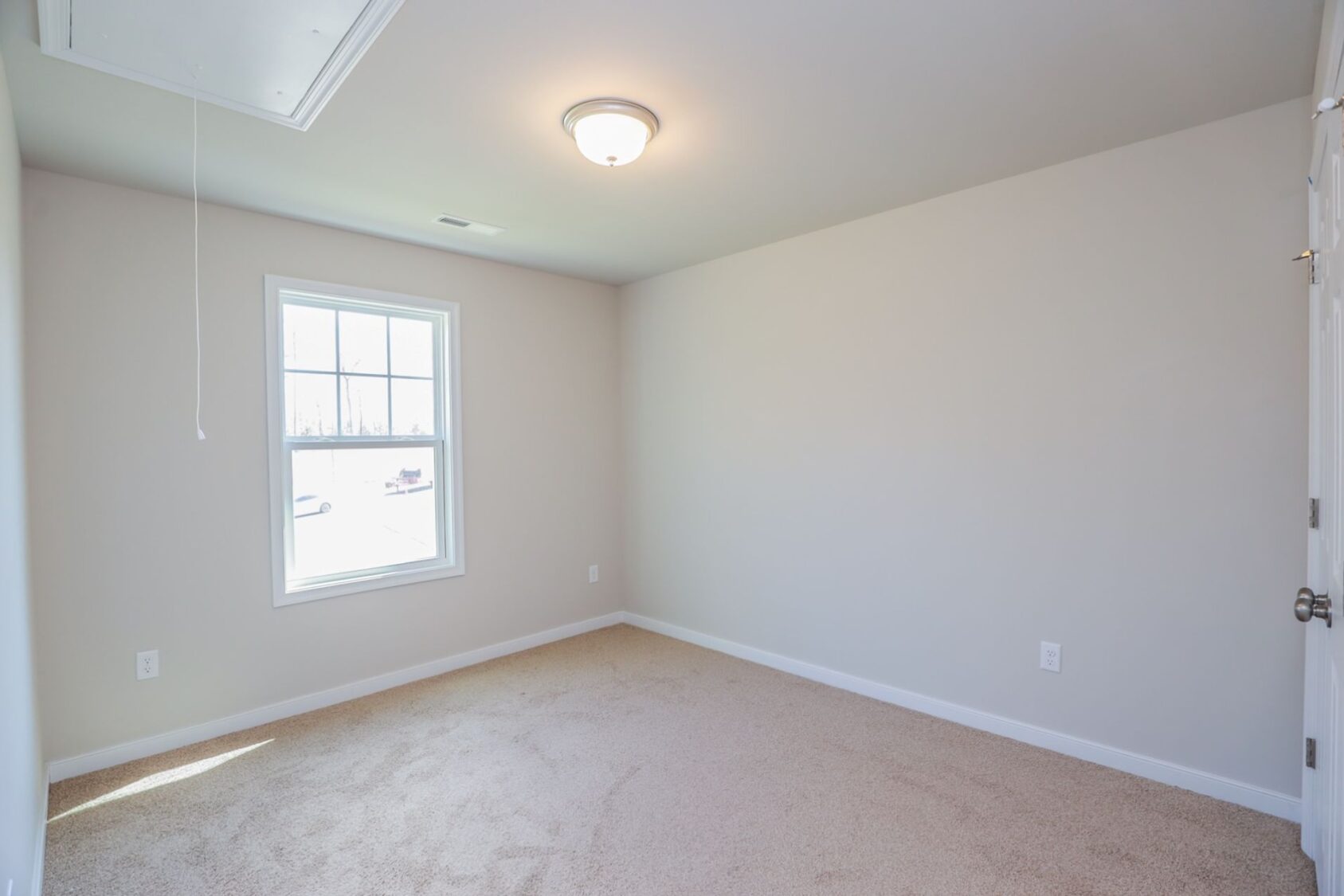 Empty room with beige carpet, light gray walls, a window, and a ceiling light fixture.
