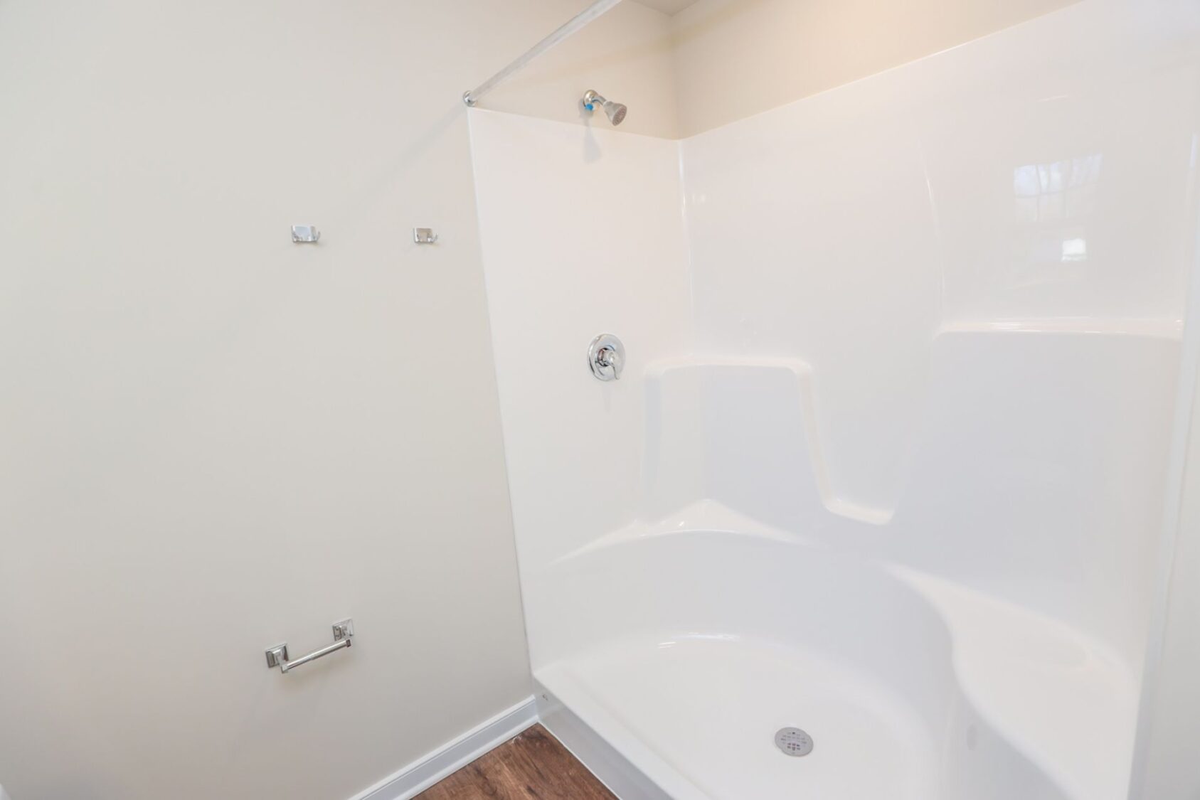 White shower and tub combo with built-in seat in a bathroom with beige walls and wood-look flooring.