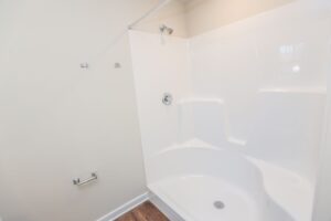 White shower and tub combo with built-in seat in a bathroom with beige walls and wood-look flooring.