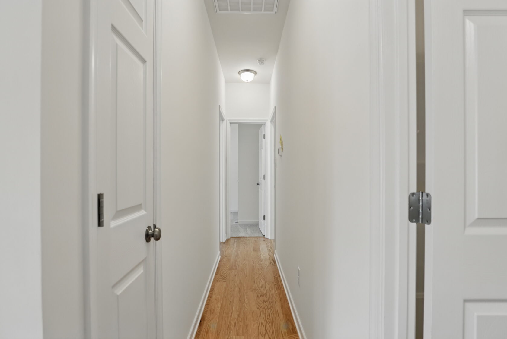A bright, narrow hallway with wooden flooring and white doors on both sides.