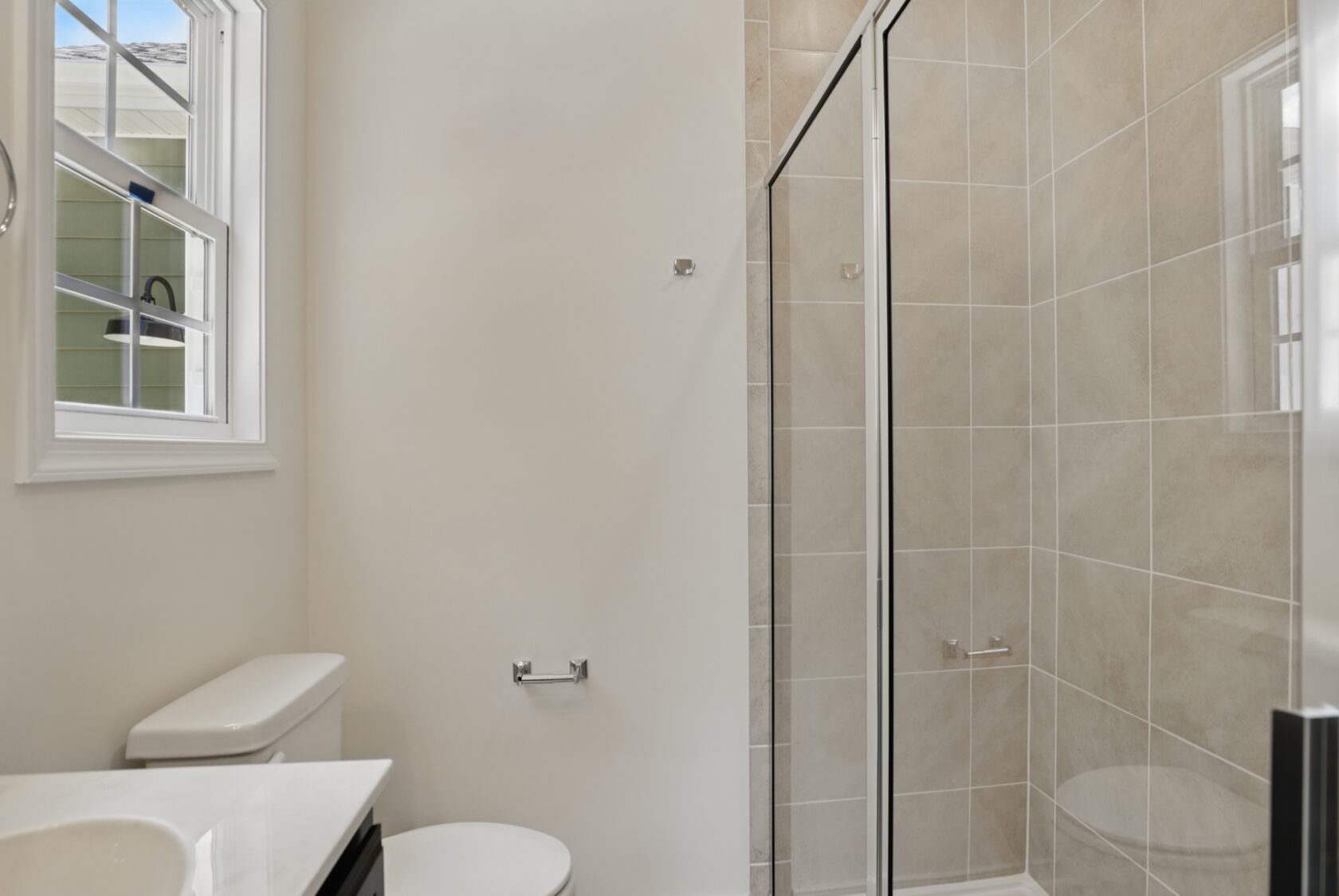 Modern bathroom with a glass shower, white toilet, tiled walls, and a window letting in natural light.