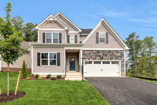Two-story Somerset Hill home with gray siding, stone accents, two-car garage, and lush grass surrounded by trees.