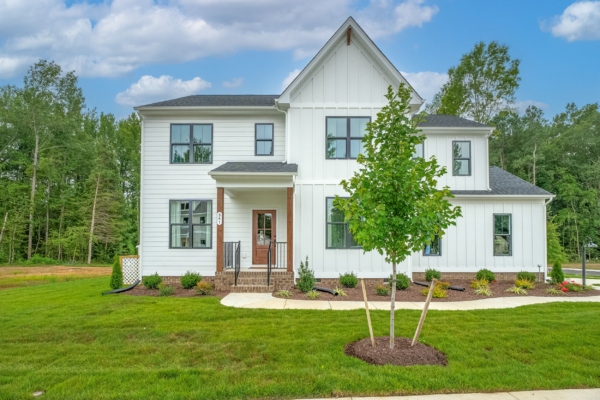 Modern white house with a gabled roof, nestled among trees and green lawn, evokes the charm of new homes in Virginia.