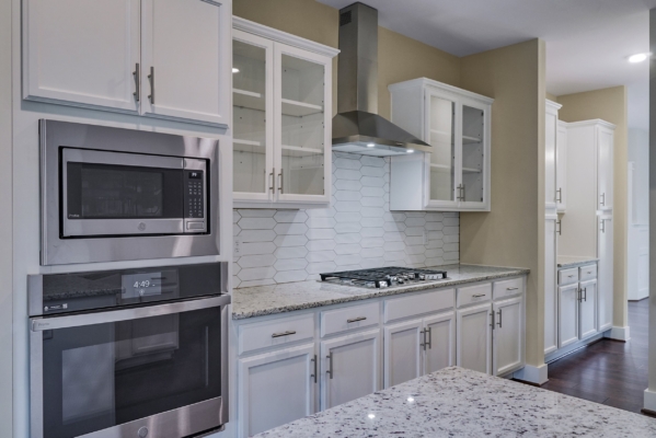 Modern kitchen with white cabinets, stainless steel appliances, a stovetop, and granite countertops.
