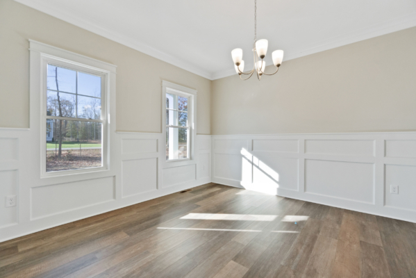 Bright room with large windows, wooden floor, beige walls, white trim, and a modern chandelier.