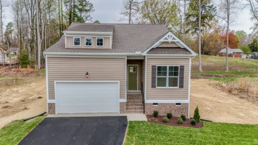 Tan two-story house with attached garage, front steps, and small landscaped yard, surrounded by trees.