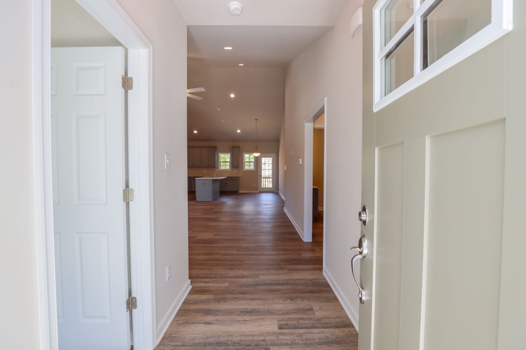 Open front door revealing a bright hallway with wooden floors leading to a spacious living area.