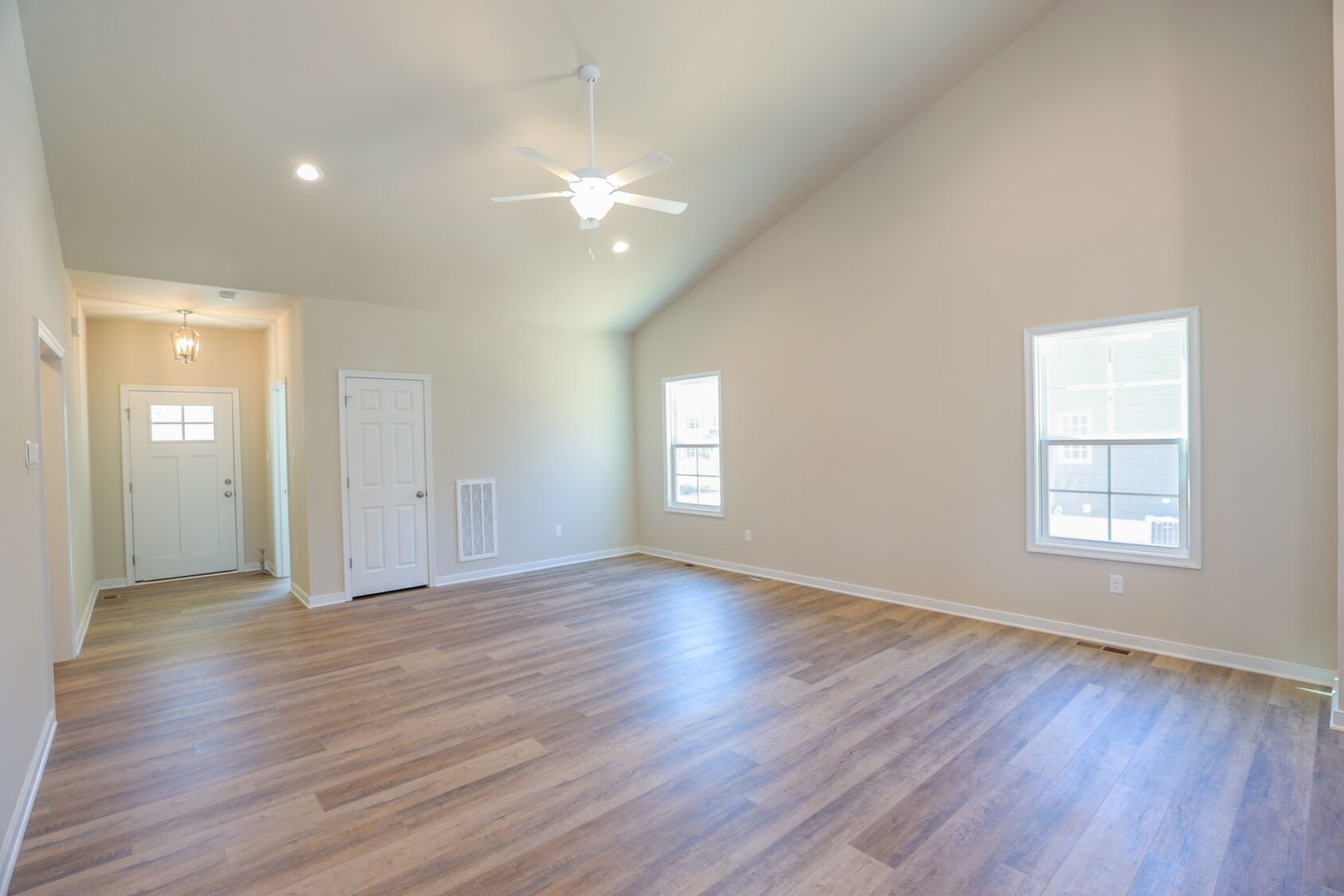 Spacious empty room with wooden floor, two windows, white door, and ceiling fan.
