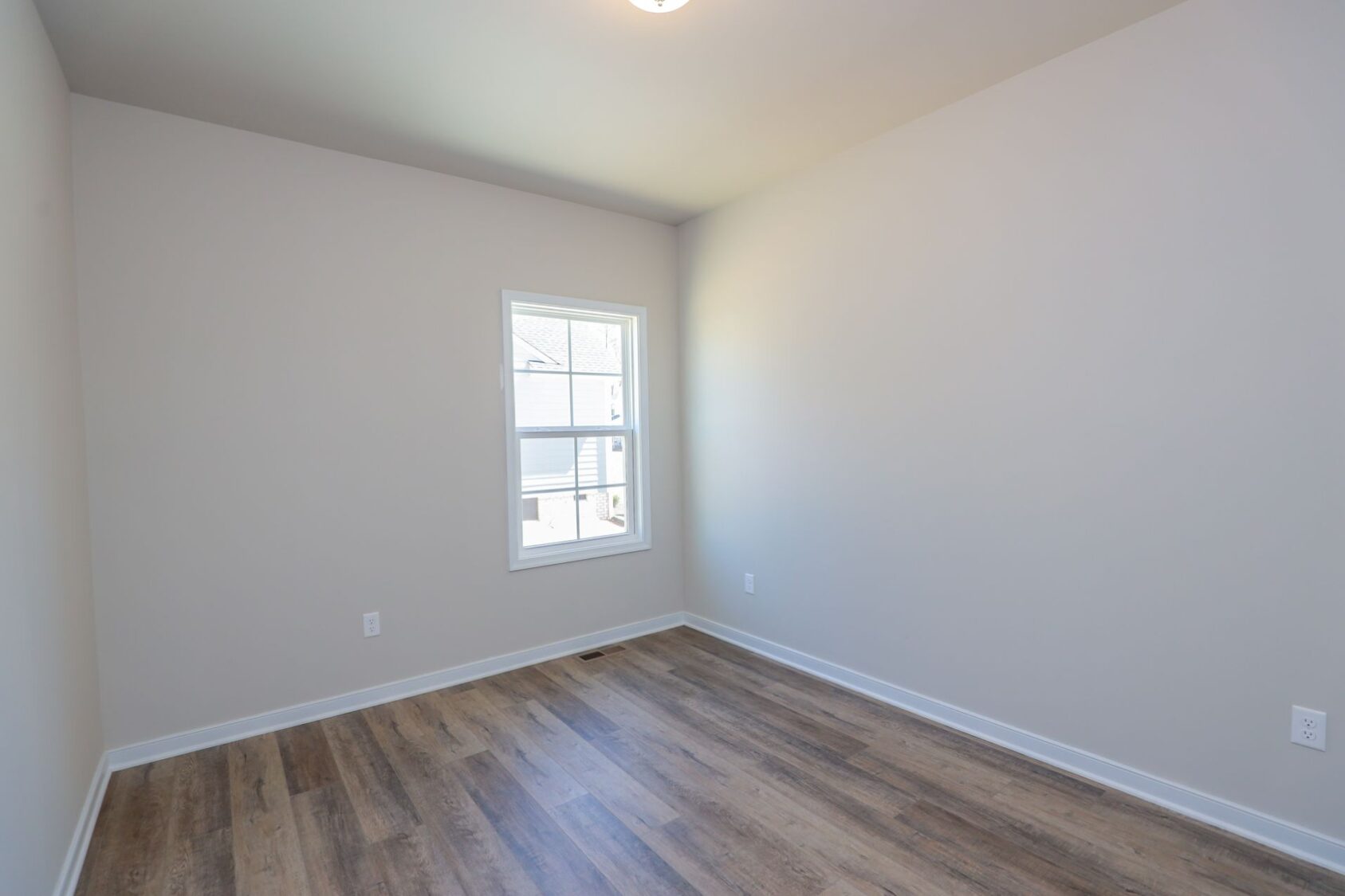 Empty room with light gray walls, wood laminate floor, and a window letting in natural light.