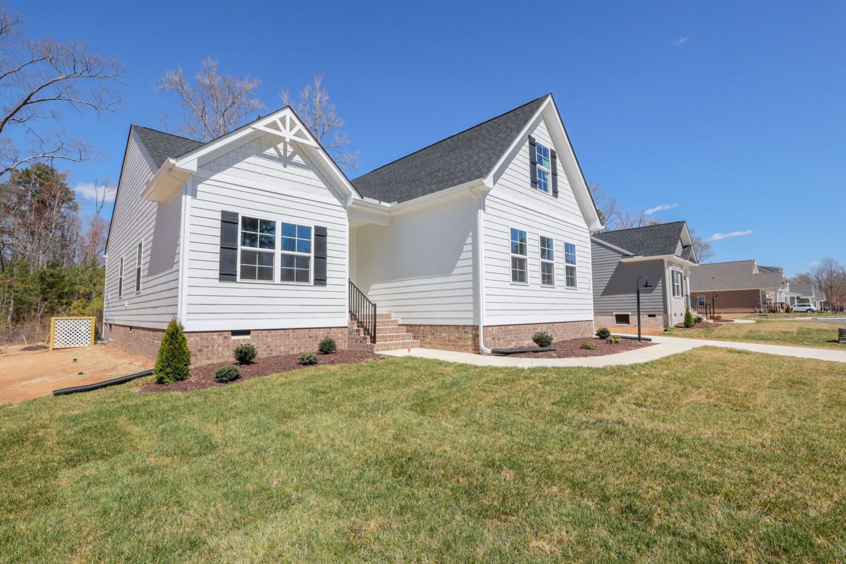 White suburban house with dark roof, surrounded by a green lawn and clear blue sky. Pathway leads to the entrance.