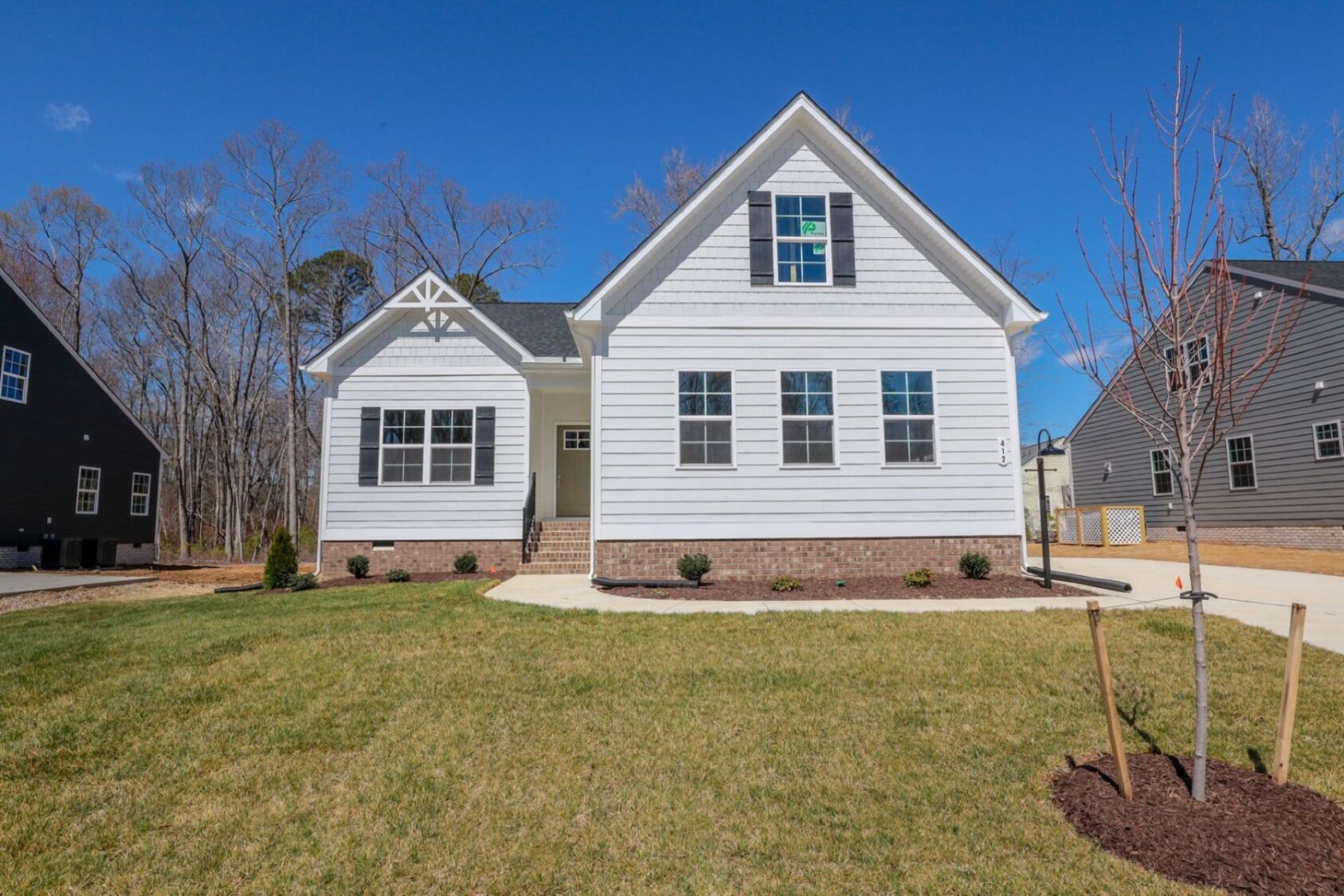 White single-story house with dormer windows, brick foundation, front lawn, and clear blue sky.