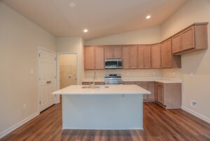Modern kitchen with wood cabinets, island with sink, stainless steel appliances, and wood flooring.