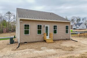 Beige single-story house with five windows, a small wooden porch, and a bare dirt yard.