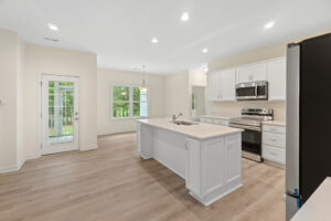 Modern kitchen at Lot 57 with a large island, stainless steel appliances, white cabinets, and wood flooring.