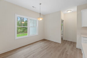 The empty room in Lot 57 boasts wooden flooring, beige walls, a large window, and a sleek hanging ceiling light.