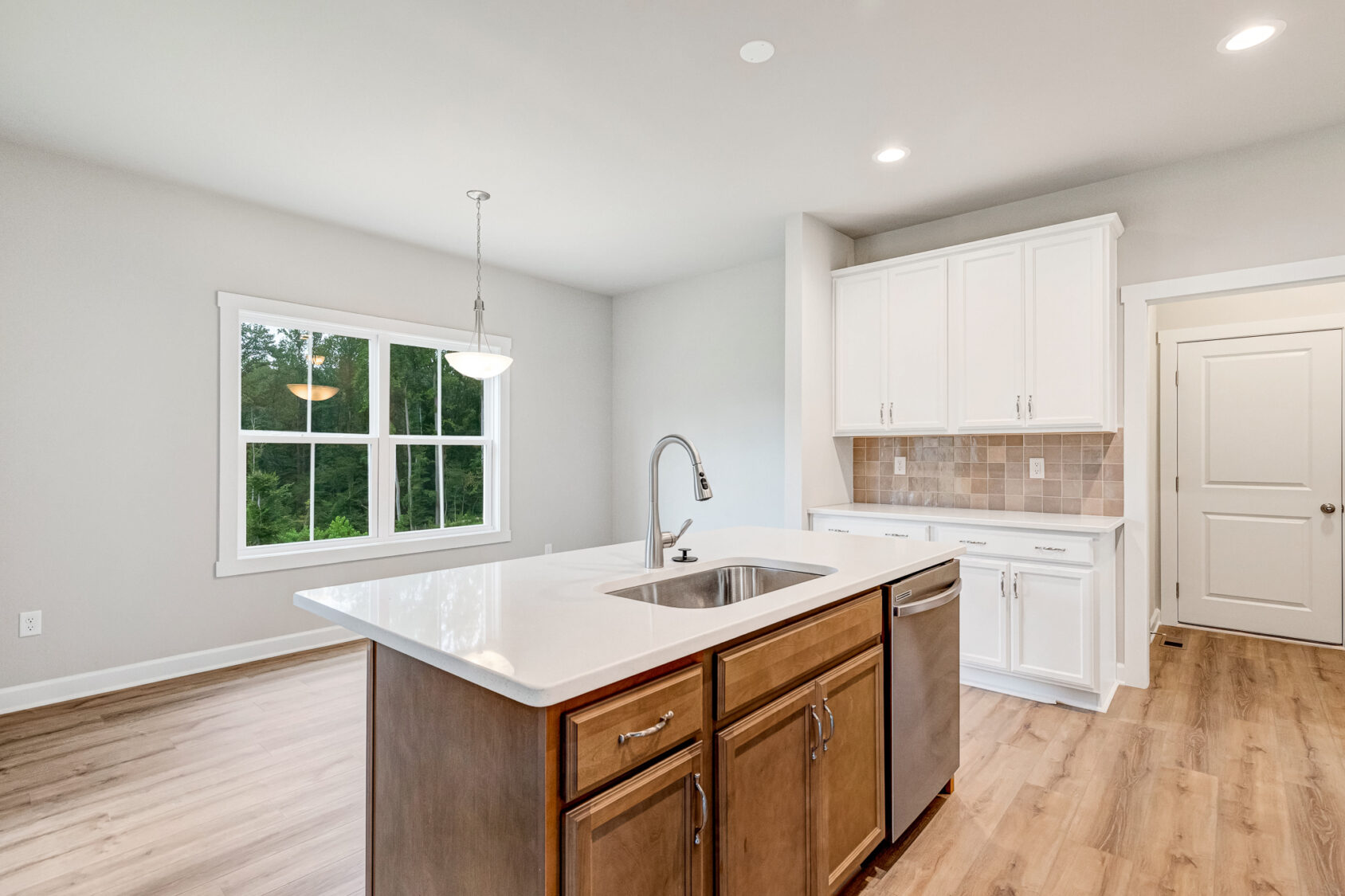 Modern kitchen with island in Poplar Village, white cabinets, wood floors, and a large window letting in natural light.
