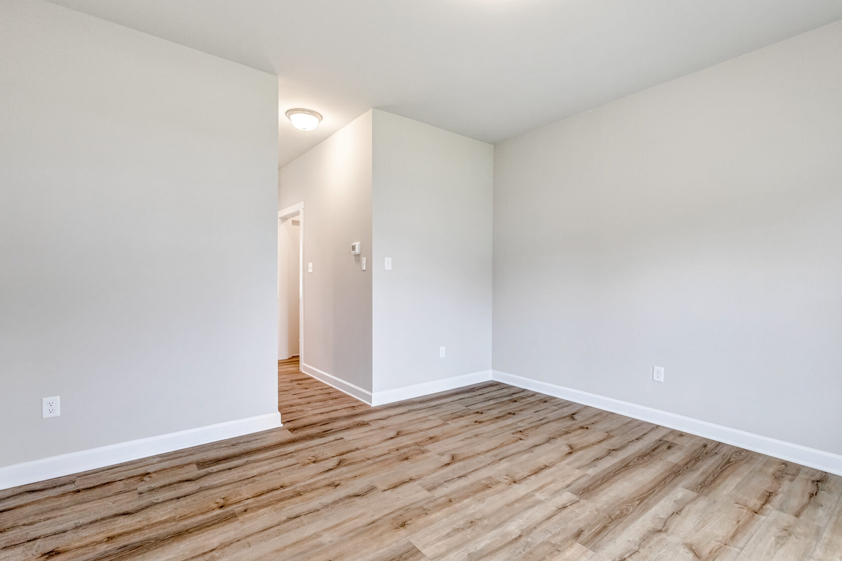 Empty room with light gray walls, wood flooring, and a hallway in Poplar Village Lot 22.