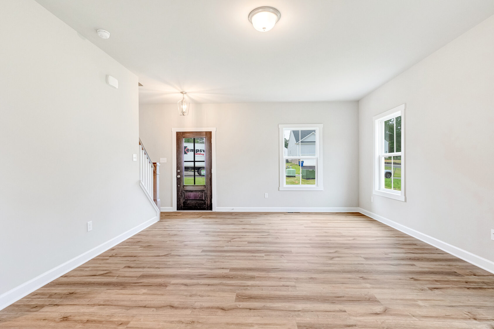Bright, empty room in Poplar Village with light wood floors, white walls, windows, and a door near a staircase.