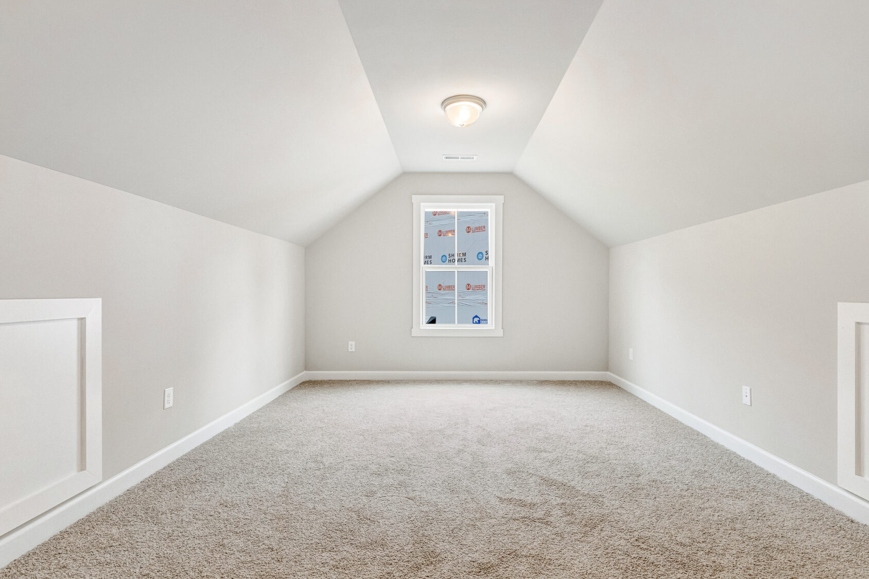 Empty, carpeted attic room with sloped ceiling in Poplar Village’s Lot 22, brightened by a single window and neutral walls.