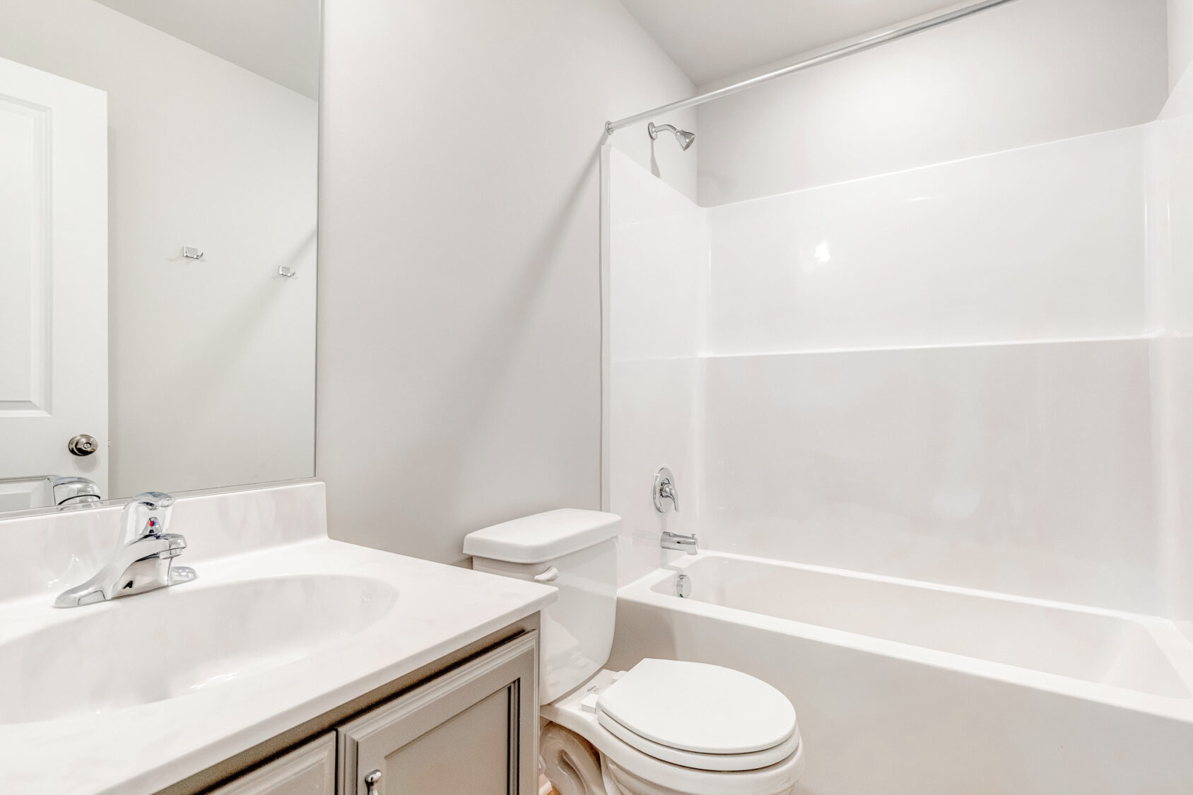 White bathroom in Poplar Villages Lot 22 with a sink, toilet, and bathtub against a light-colored wall.