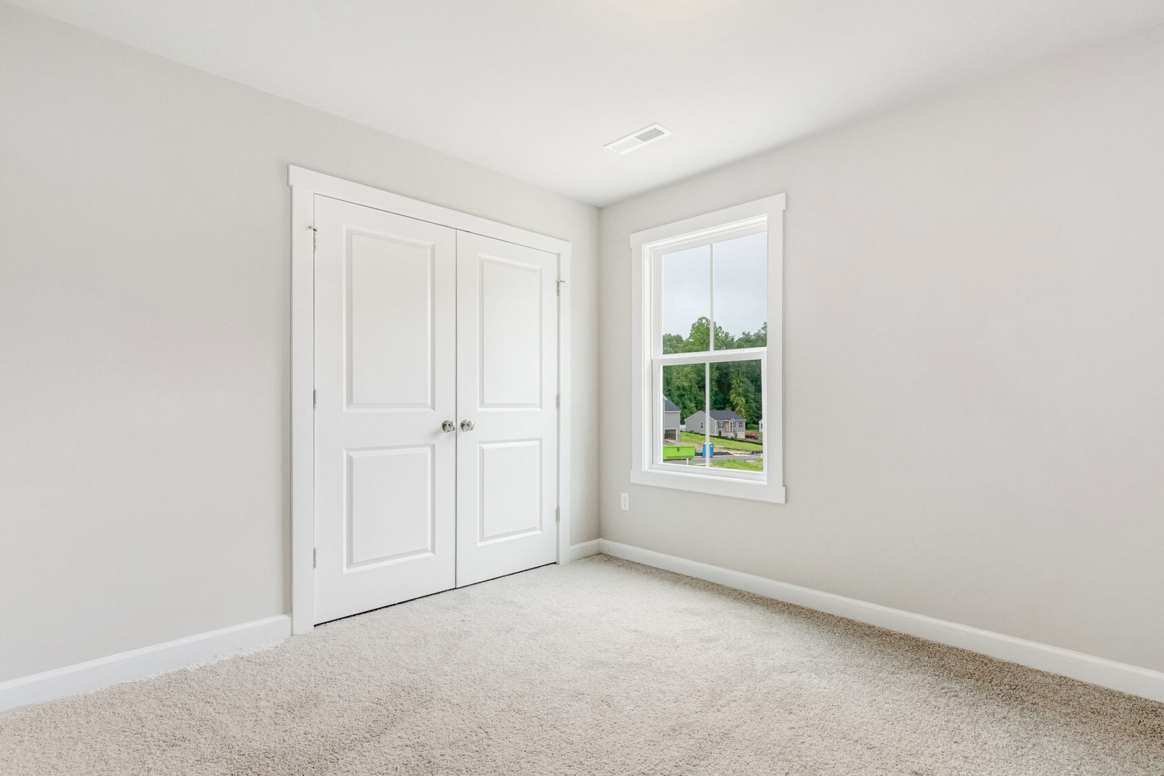 Empty room in Poplar Village with beige carpet, double closets, and a window offering a suburban view.