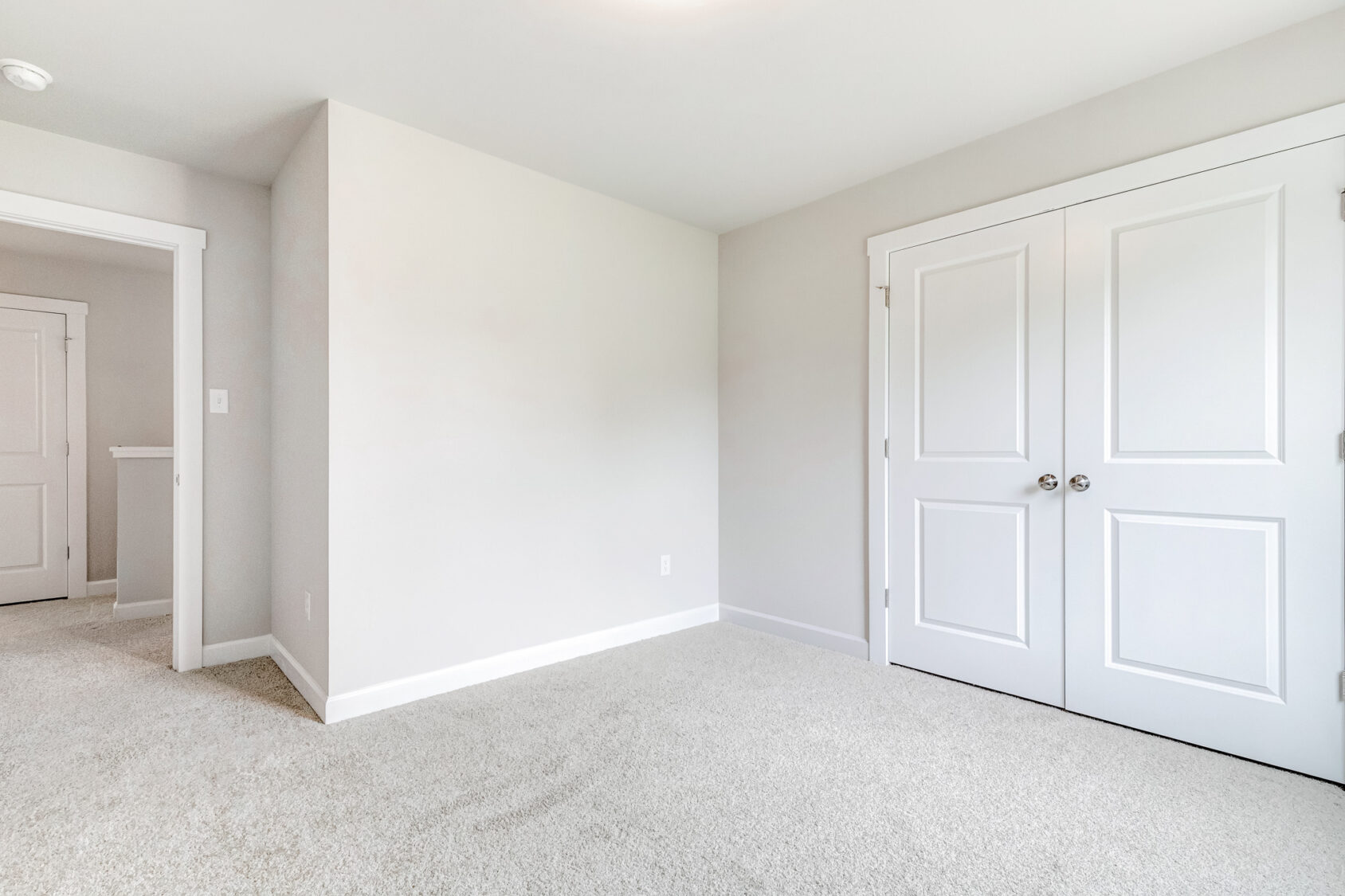 Empty room in Poplar Village with beige carpet, white walls, double closet doors. Door opens to hallway. Lot 22.