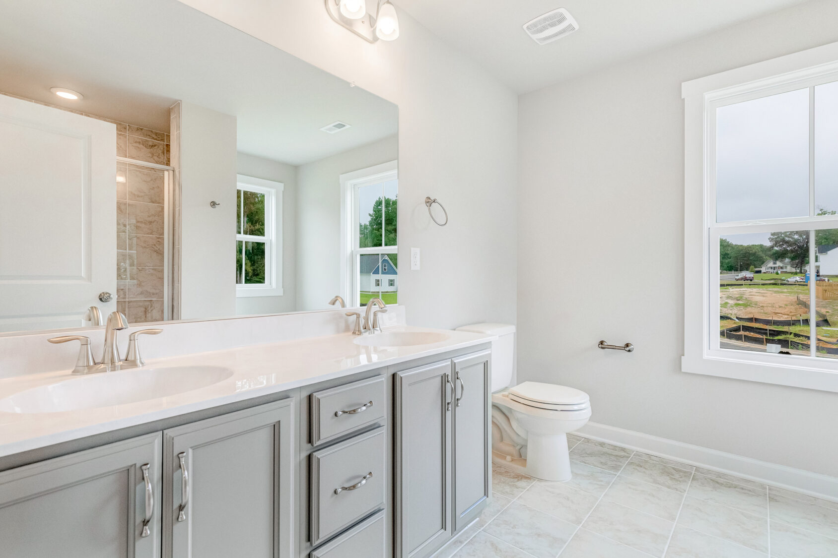 Bright Poplar Village bathroom on Lot 22 with gray cabinets, double sinks, large mirror, and windows with outdoor views.