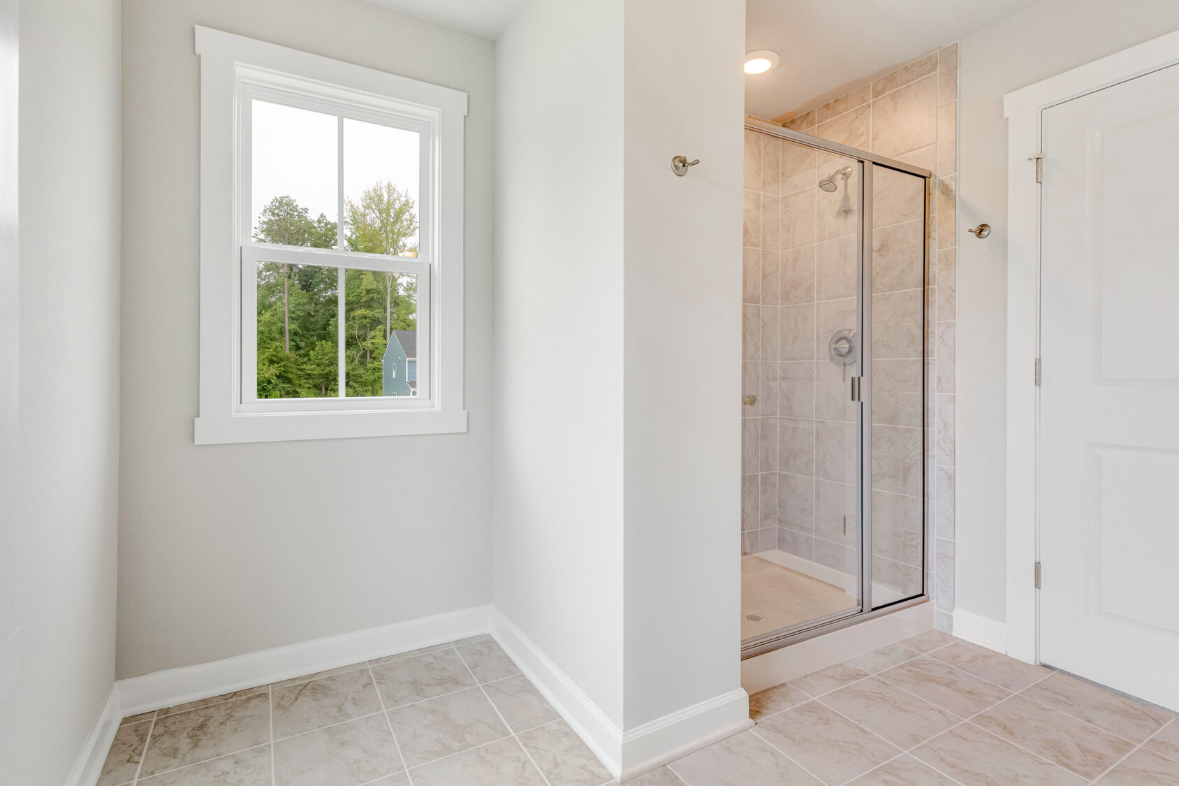 Bright bathroom in Lot 22, Poplar Village with tiled floor, glass shower, white walls, and a window showing greenery.